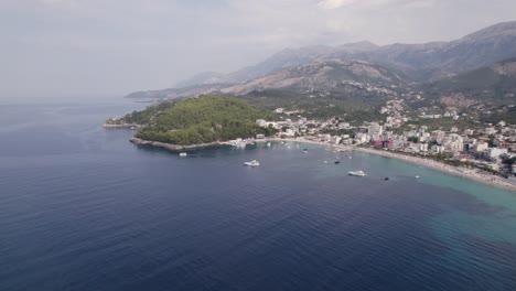 Drone-view-from-over-the-Ionian-Sea-of-the-Ceraunian-mountains,-overlooking-the-beautiful-beach-town-of-Himare,-Albania