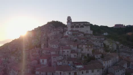 Mountain-slope-village-Artena-with-church-morning-sunlight-peaking-from-hill-edge,-aerial