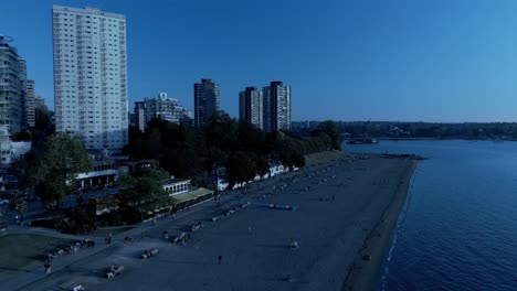 English-Bay-Sunset-Beach-reveal-pan-drone-overlooking-commercial-properties-of-Davie-and-Denman-pubs-restaurants-condominiums-apartments-hotels-shops-sunny-summer-day-skyline-lush-greenery-post-modern