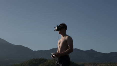 Young-Man-With-Goggles-and-Remote-Controlling-FPV-Drone-Flying-By-in-Outdoors