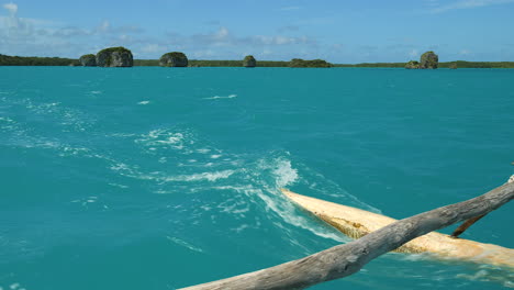 Traditional-outrigger-canoe,-or-pirogue,-sails-Upi-Bay,-floating-rocks-in-distance
