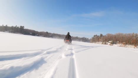 FPV-drone-following-person-driving-snowmobile-on-a-frozen-lake-covered-with-thick-snow-during-the-day