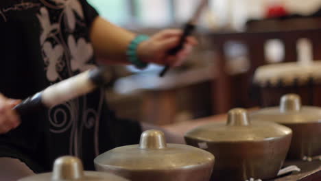 Wooden-mallet-being-used-to-strike-multiple-south-east-Asian-bonang-drums-during-gamelan-performance,-filmed-as-close-up-in-handheld-style