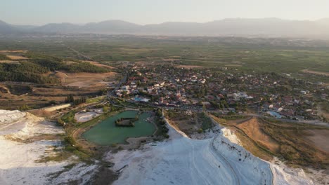 Aerial-View-of-Pamukkale-Town-Turkey-Under-White-Limestone-Hills,-Popular-Tourist-Destination-on-Sunny-Day,-Drone-Shot