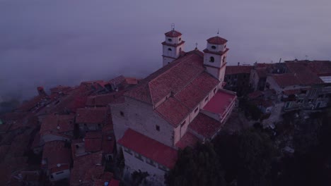 Iglesia-En-La-Cima-De-La-Colina-Con-Impresionantes-Vistas-Del-Valle-Lleno-De-Niebla-Al-Amanecer,-Antena