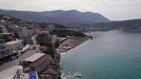 Aerial-of-Himare,-Albania's-coastal-road,-crystal-clear-sea,-and-majestic-mountains
