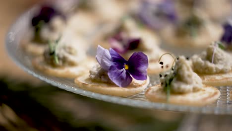Edible-violet-flower-on-top-of-cracker-vegan-appetizer-tapas-bites,-Close-up-shot