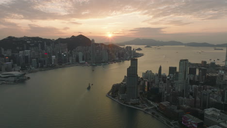 Aerial-drone-shot-of-Tsim-Sha-Tsui-district-with-Rosewood-Hotel,-K11-in-the-foreground-and-Hong-Kong-Island-in-the-background-during-sunset