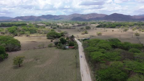 Advancing-grey-vehicle-on-dirt-road-in-Costa-Rica-near-farmland,-Aerial-dollyout-shot