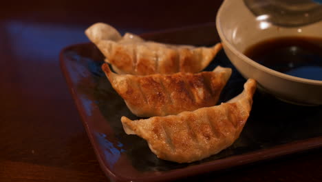 Restaurant-gyoza-pan-fried-dumpling-pot-stickers-plated-with-soy-dipping-sauce,-slider-close-up-4K