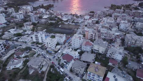 Drohnen-Überführung-über-Die-Innenstadt-Von-Ksamil,-Die-Einen-Atemberaubenden-Sonnenuntergang-über-Der-Ionischen-Meereslandschaft-Enthüllt,-Aufnahme-Nach-Oben-Geneigt