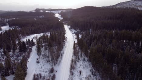 Very-fast-descending-drone-shot-over-winter-road-covered-with-snow-and-surrounded-with-forest