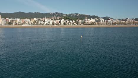 Orbits-over-a-solo-stand-up-paddle-surf-with-a-view-of-the-town-in-the-background,-on-a-sunny-autumn-day