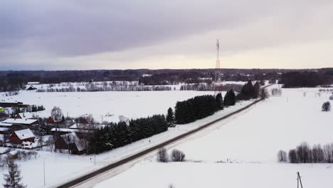 Telecommunication-tower-in-small-snow-covered-village-on-overcast-winter-day,-aerial-view