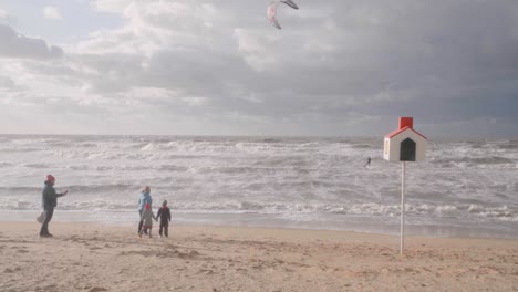 Back-view-of-family-near-the-North-Sea,-watching-kiteboarder-on-windy-outdoors-background---Belgium