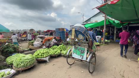 Toma-En-Gran-Angular-De-Los-Vendedores-Del-Mercado-Local-De-Verduras-Al-Borde-De-La-Carretera-Que-Venden-Verduras-Mientras-El-Rickshaw-Cruza-Por-El-Medio,-Dhaka,-Bangladesh