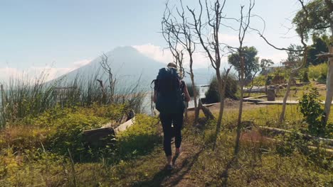 Two-backpackers-walk-with-their-bags-on-the-shores-of-lake-Atitlan,-Guatemala,-in-the-sun