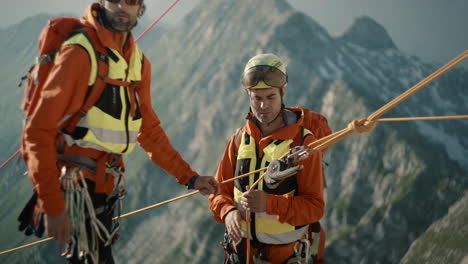 Two-hikers-in-orange-climbing-gear-tieing-ropes-for-a-secure-descent-down-to-the-valley