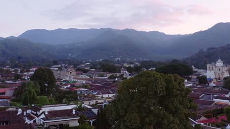 Drone-shot-reveals-San-Francisco-the-Great-basilica-in-Antigua,-Guatemala,-at-sunrise,-with-pink-clouds-and-blue-mountains-in-the-background