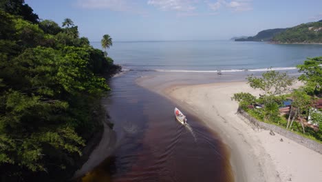Aerial-view-following-a-boat-leaving-a-river-towards-the-ocean-in-Barra-Do-Sahy,-Brazil