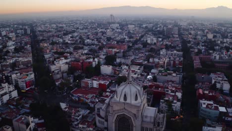 Wide-drone-shots-of-massive-Jesus-status-towering-over-Mexico-City-at-sunset,-featuring-Parroquia-del-Purism-Corazon-de-Maria-and-straight-streets-in-the-background