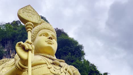 Low-angle-shot-of-close-up-of-a-golden-statue-of-Hindu-god-Murugan-outside-of-Subramanya-temple-along-Batu-Caves,-Malaysia