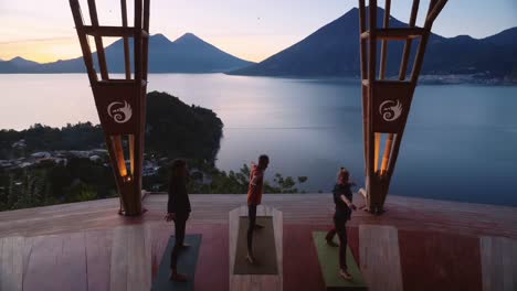 Three-people-practice-yoga-at-sunrise-on-a-platform-overlooking-lake-Atitlan-in-Guatemala