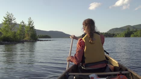 Female-paddles-a-canoe-on-a-lake-with-mountains-in-the-background-during-sunset-in-slow-motion
