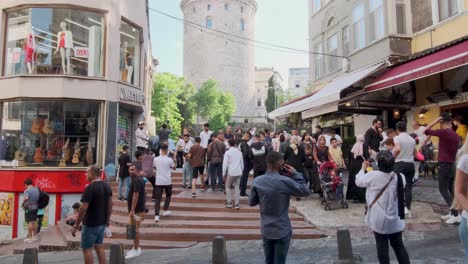 Tilt-Shot-Aufnahmen-Zeigen-Den-Ikonischen-Galata-Turm-In-Istanbul,-Türkei,-Mit-Touristen,-Die-An-Einem-Sonnigen-Morgen-Durch-Die-Straßen-Wandern