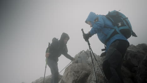 Zwei-Wanderer,-Die-Den-Gipfel-Des-Berges-Erreichen,-Ruhen-Sich-Bei-Windigen-Bedingungen-Und-Niedriger-Wolkendecke-Aus