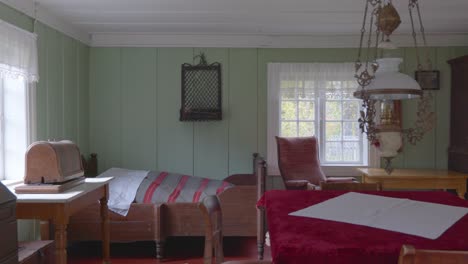 Pan-shot-inside-a-traditional-Norwegian-wooden-cottage-bedroom,-showcasing-old-fashioned-bed,-wooden-flooring-and-furniture