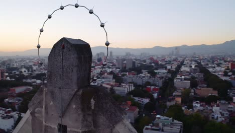 Dramatic-cinematic-wide-drone-shots-of-massive-Jesus-status-towering-over-Mexico-City-at-sunset,-featuring-Parroquia-del-Purism-Corazon-de-Maria-and-the-sun-setting-over-mountains-and-buildings