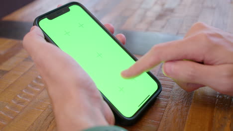 Cinematic-shot-of-person-holding-an-iPhone-with-green-screen-display,-tapping-and-swiping-on-the-screen