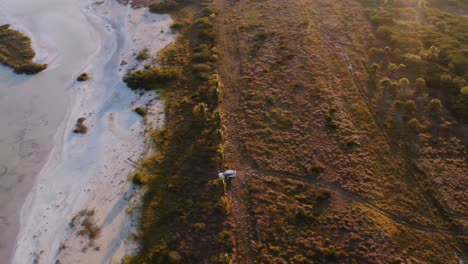 Wide-dynamic-drone-shot-of-white-overland-vehicle-parked-on-the-shore-of-a-lake-in-Progreso-Yucatan-Mexico-as-the-sun-sets