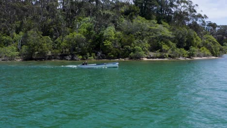 A-beautiful-total-view-tracking-shot-of-a-small-boat-at-the-coastline-of-Australia,-with-a-sunny-day,-trees,-sea,-and-daylight