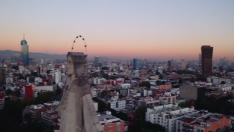 Wide-establishing-drone-shot-of-massive-Jesus-status-towering-over-Mexico-City-at-dusk-after-sunset,-featuring-Parroquia-del-Purism-Corazon-de-Maria-and-buildings-in-the-back