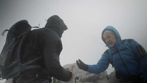 Two-hikers-reached-the-top-of-the-mountain,-congratulatind-eachother-and-signing-a-direction-they-will-take