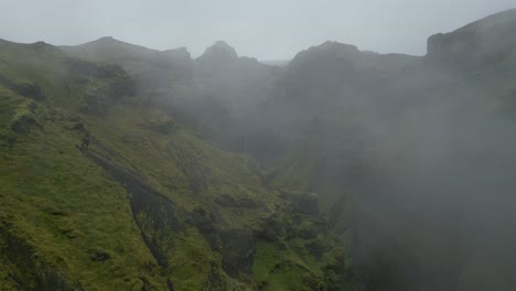 Cinematic-establishing-shot-flying-through-mist-revealing-a-canyon-valley-and-waterfall
