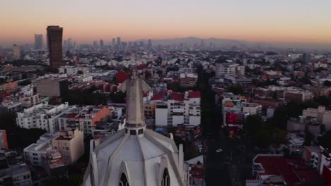 Dynamic-wide-swooping-drone-shots-of-massive-Jesus-status-towering-over-Mexico-City-at-sunset,-featuring-Parroquia-del-Purism-Corazon-de-Maria-and-buildings-in-the-back