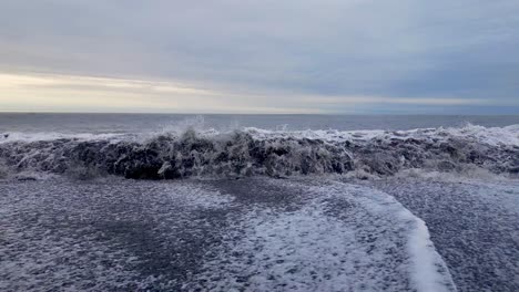 Surf-waves-forming-white-foam-crashing-onto-a-black-sandy-beach
