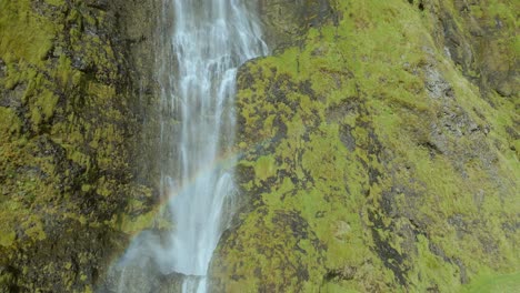 Drone-pan-up-of-a-waterfall-cascading-over-large-yellow-moss-cliffs