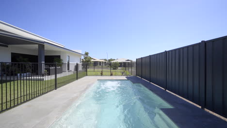 Large-luxurious-contemporary-outdoor-swimming-pool-in-ground,-clear-blue-water-black-fence-grey-tiled-decking-close-up-of-pool-spa-modern-home-green-grass-blue-skies