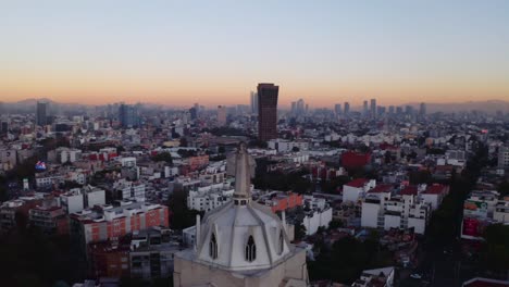 Wide-drone-shots-of-massive-Jesus-status-towering-over-Mexico-City-at-sunset,-featuring-Parroquia-del-Purism-Corazon-de-Maria-and-buildings-in-the-back