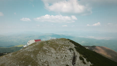 Drone-shot-of-top-of-the-Snežnik-mountain-with-a-half-hidden-mountain-cottage-with-red-roof