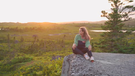 Woman-sitting-on-rocks-in-the-wilderness-in-golden-hour-sunset-smiling