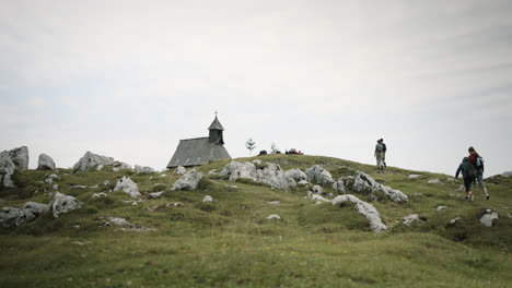 People-walking-towards-the-church-on-the-top-of-mountain-Velika-planina,-rocks-sticking-out-of-the-earth