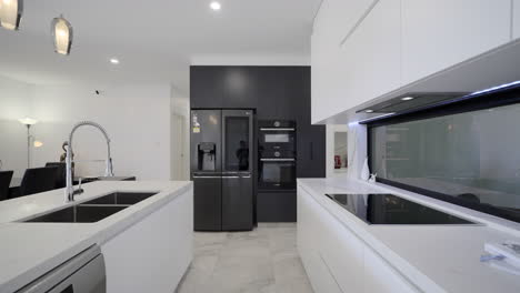 Modern-Luxurious-Contemporary-kitchen-white-marble-bench-top-drop-lighting-marble-tiled-floors-black-feature-wall-with-sleek-black-appliances-fridge-white-kitchen-storage-red-appliances