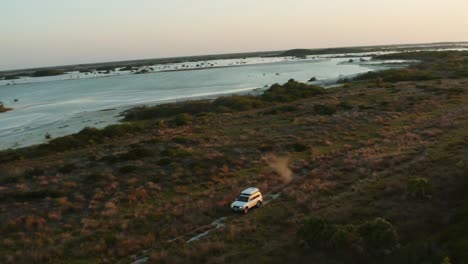 Dynamic-wide-aerial-shot-of-all-terrain-SUV-with-a-rooftop-tent-riding-through-a-rough-field-and-kicking-up-dust