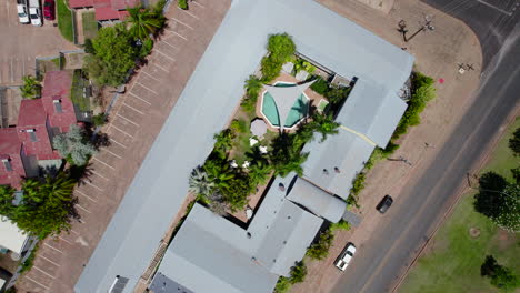 Aerial-Drone-Luxurious-Property-Birds-eye-view-of-round-outdoor-pool-Tropical-greenery-palm-trees-grey-shade-sail,-outdoor-seating-entertainment-area,-sun-lounge-grey-roofs