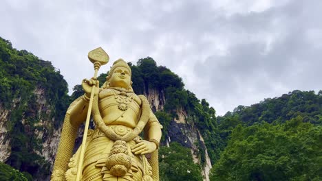 Low-angle-shot-of-golden-statue-of-Hindu-God-Murugan-in-front-of-Subramanya-temple-with-the-view-of-steep-mountain-cliff-in-the-background-in-Malaysia